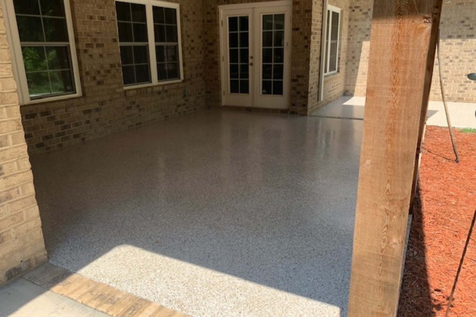 epoxy coated covered patio with sandstone flake finish at brick home exterior