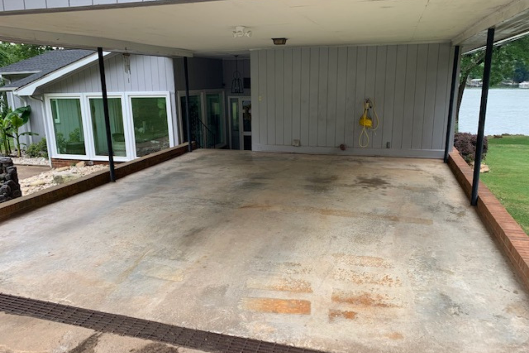 covered lakeside carport with stained concrete slab and visible surface wear before epoxy coating